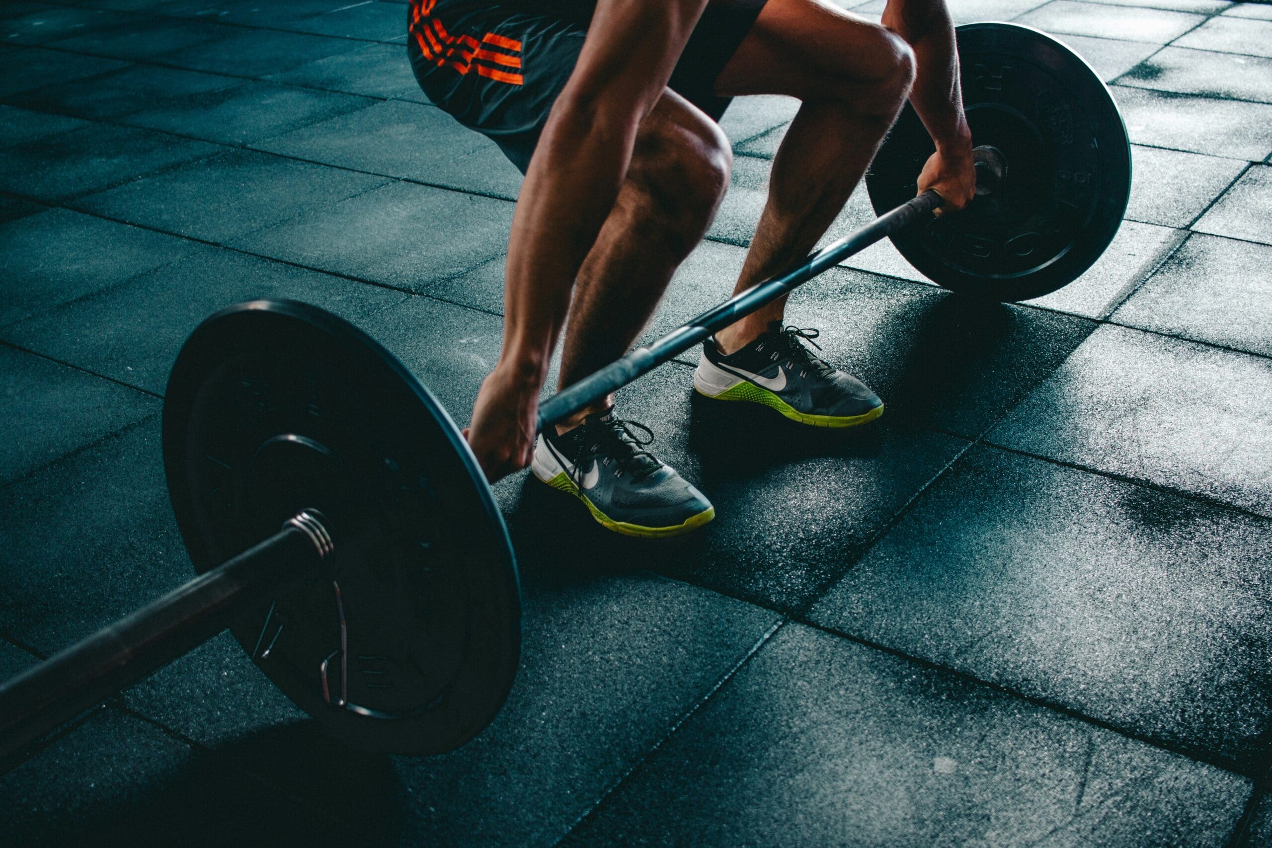 picture of a woman squatting down to pick up a barbell with weights in the gym